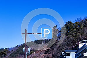 Parking (P) sign mounted on brown steel beam. Mountains, blue sky and bright sunlight in the background.