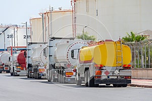 Parking row jam of trucks with fuel tanks in front of a warehouse and storage of huge tanks of raw material containers