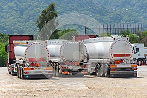 Parking row jam of trucks with fuel tanks in front of a warehouse and storage of huge tanks of raw material containers, next to