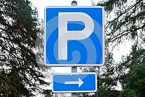 Parking sign with arrow in the park on sky and trees background