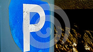 Parking sign with P lettering on blue background on parking ticket machine, with wall in background