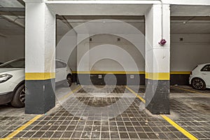Parking spaces delimited with yellow paint on the ground floor of a building with a garage and parked vehicles