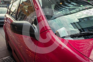 Parking ticket under windshield on a red car in an urban city environment