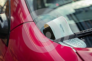 Parking ticket under windshield on a red car in an urban city environment