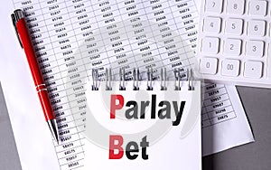 PARLAY BET text on notebook with pen, calculator and chart on grey background