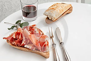 Parma flavored ham in spices, thinly sliced on a white table with red wine bread and antique cutlery