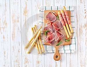 Parma ham prosciutto with Italian grissini breadsticks on a white wooden table, top view