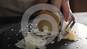 Parmesan cheese composition, on a wooden cutting board. One hand takes the knife and breaks a couple of pieces to savor