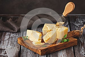 Parmesan cheese on a cutting board with basil leaves, rustic wooden table. Selective focus, dark background