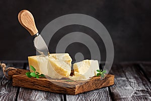 Parmesan cheese on a cutting board with basil leaves, rustic wooden table. Selective frus