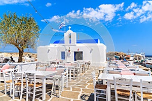 Tavern tables on square with typical white Greek church in Naoussa port, Paros island, Cyclades, Greece
