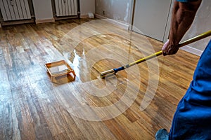Parquet floor renovation. Lacquering wood floors. Worker uses a roller to coating floors