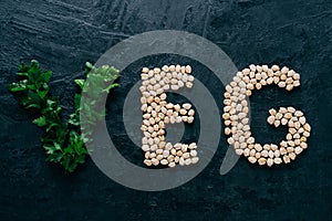 Parsley and dry garbanzo in form of letters meaning veg, vegetarian isolated over dark background. Organic protein product. Vegan photo