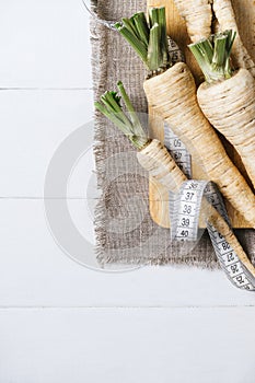 Parsley root with a measuring tape and tomatoes on cutting board on a white background of the old wooden boards vintage top view v