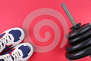 Part of a barbell with disks and sports sneakers flat lay on a red background
