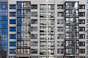 Part of beige wall with a group of blue windows and balconies with reflections. Horizontal texture of colored windows on