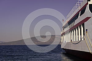 Part of big cruise liner in sea at sunny day. Cruise ship sailing from port. Skyline with mountains and ocean, horizon