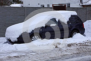 Part of a blue passenger car under a snowdrift of white snow on the street