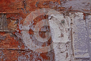 Part of a brick wall with peeling white, gray and red paint