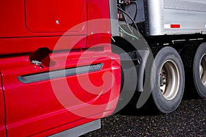 Part of bright red semi truck with aluminum trailer with wheels