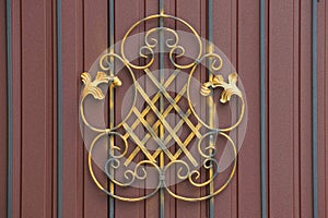 Part of a brown metal fence with black steel rods and a forged pattern of yellow color