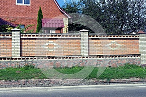 Part of a brown white brick fence wall on a gray stone foundation