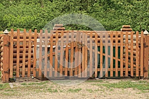 part of a brown wooden fence with a closed gate made of boards in front of the garbage cans