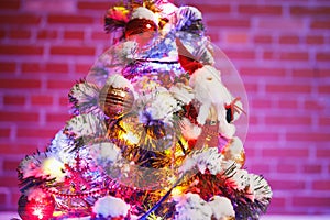 Part of Christmas tree with festive lights in snow outdoors, purple brick wall background