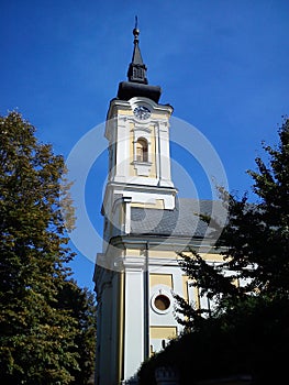 Part of the church building with a dome and a clock under it. The temple is painted in white - yellow colors, the dome and spire