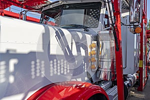 Part of classic big rig white semi truck tractor with red accents and car hauler semi trailer standing on the warehouse parking