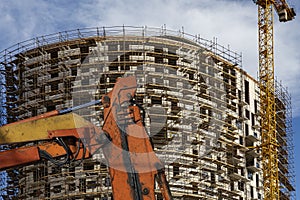 Part of a construction machine with multi-storey building under construction with scaffolding on the background