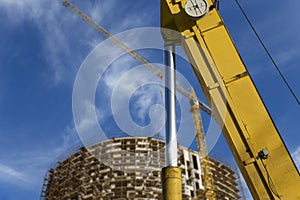 Part of a construction machine with multi-storey building under construction with scaffolding on the background