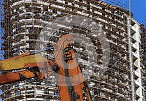 Part of a construction machine with multi-storey building under construction with scaffolding on the background