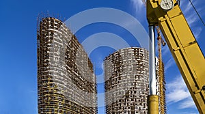 Part of a construction machine with multi-storey building under construction with scaffolding on the background