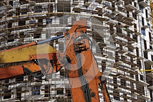 Part of a construction machine with multi-storey building under construction with scaffolding on the background