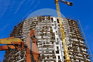 Part of a construction machine with multi-storey building under construction with scaffolding on the background