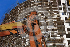 Part of a construction machine with multi-storey building under construction with scaffolding on the background