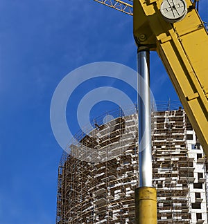 Part of a construction machine with multi-storey building under construction with scaffolding on the background