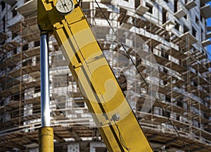 Part of a construction machine with multi-storey building under construction with scaffolding on the background