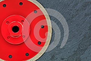 A part of a diamond cutting wheel is red with a threaded nut on a background of gray granite