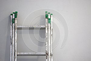 Part of dirty aluminum ladder against the background of a white wall.
