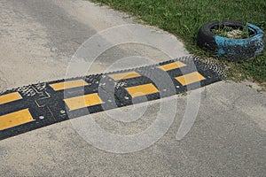 Part of dirty black yellow speed bump on gray asphalt road