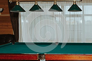 Part of an empty billiard table and lamps above it