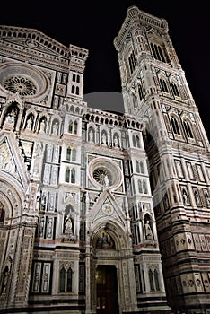 Part of the facade of the cathedral of Santa Maria in Fiore, with Giotto`s bell tower to the right, illuminated in a black backgro