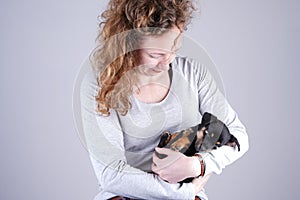 Part of a female, she lovingly holds a tiny sleeping Jack Russel Terrier puppy in her arms