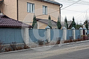 Part of a fence of gray metal and brick with a closed brown door on a winter street