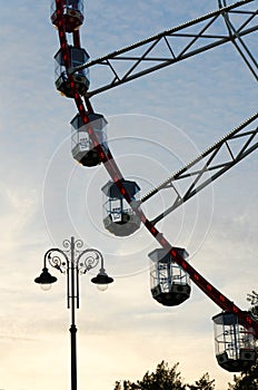 Part of ferris wheel with cabins and lamppost at sunset sky background.