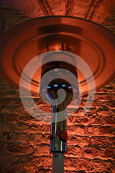 Part of a gas burning patio heater from stainless steel metal against a red illuminated rustic brick wall, selected focus