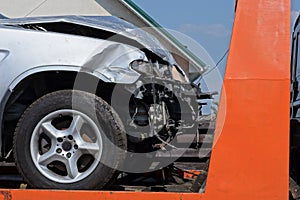 part of a gray broken passenger car after an accident stands on the orange metal of a tow truck