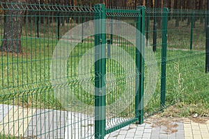 part of a green fence made of metal rods in a net and a closed door
